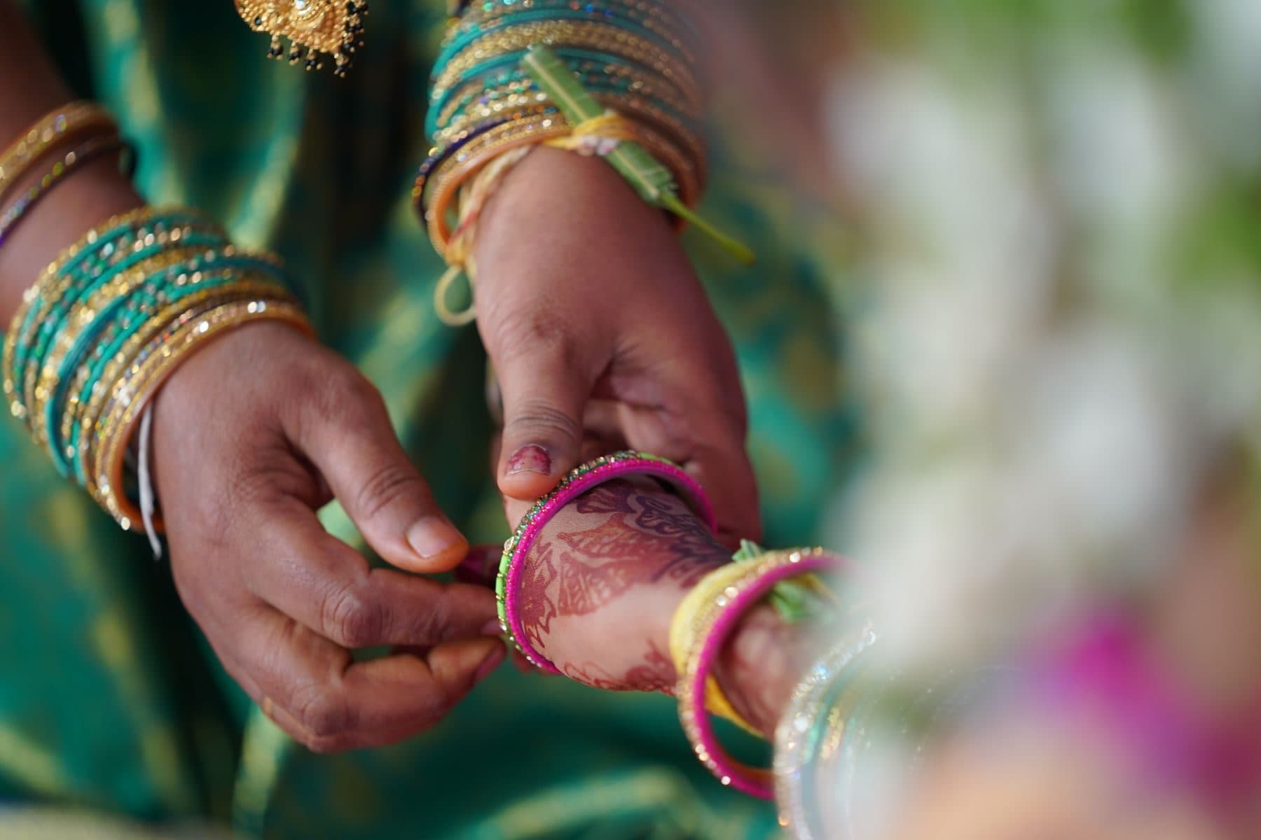 A green glass bangle being slipped onto a mehendi-decorated wrist at a godh bharai