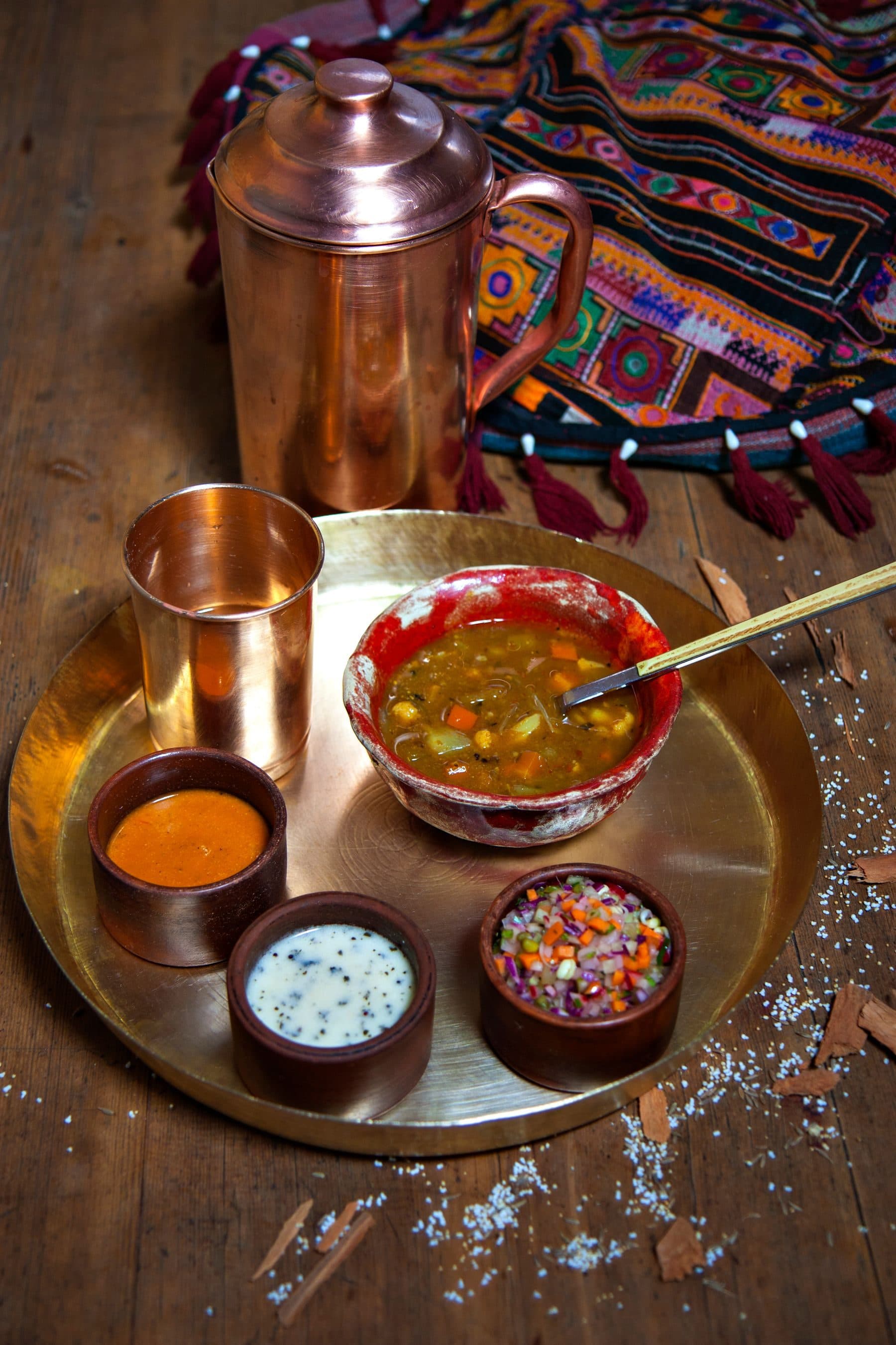 A brass thali with a copper tumbler and dal on a wooden table