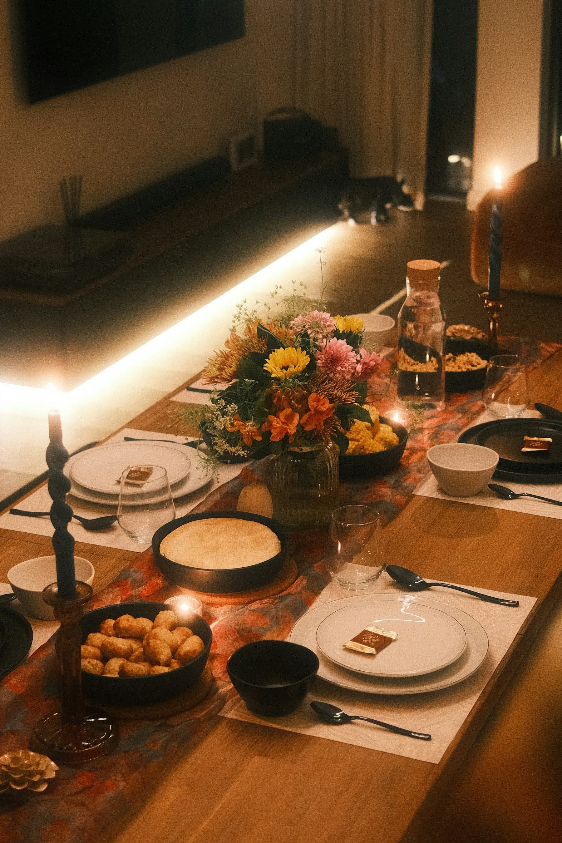 A long dinner table set with candles and flowers in a dimly lit living room