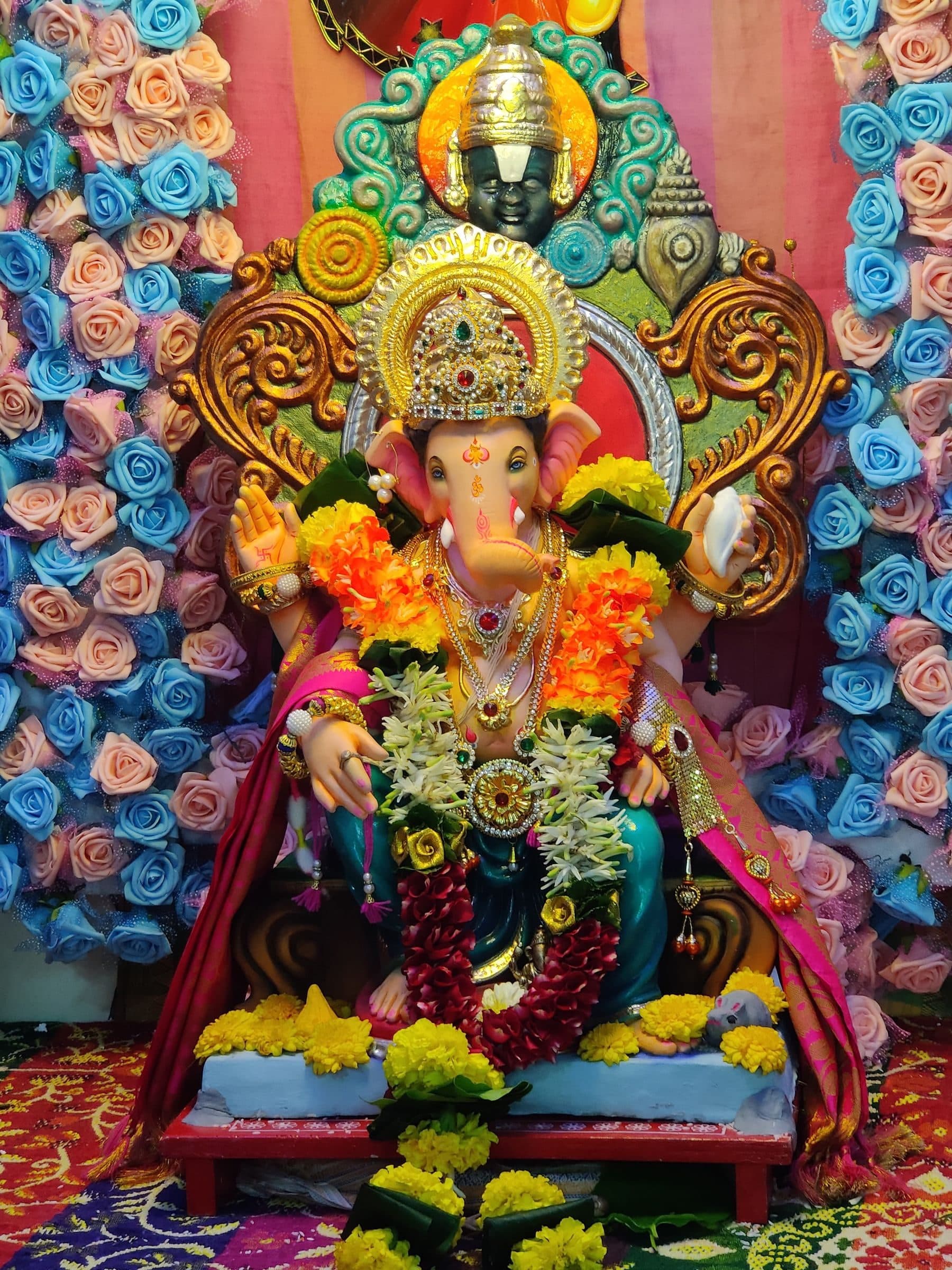 A Ganpati idol dressed in marigolds against a wall of pink and blue flowers