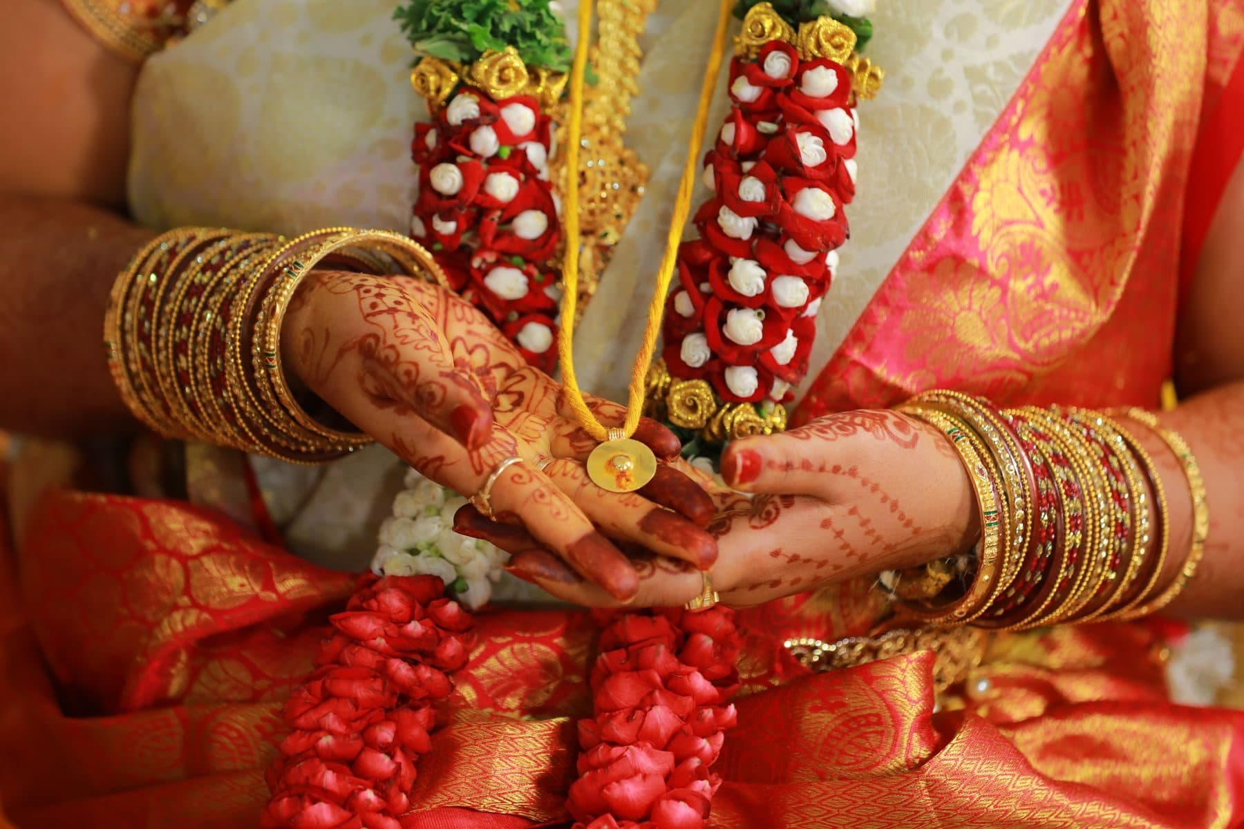 Mehendi-decorated hands with bangles holding a jasmine and rose garland