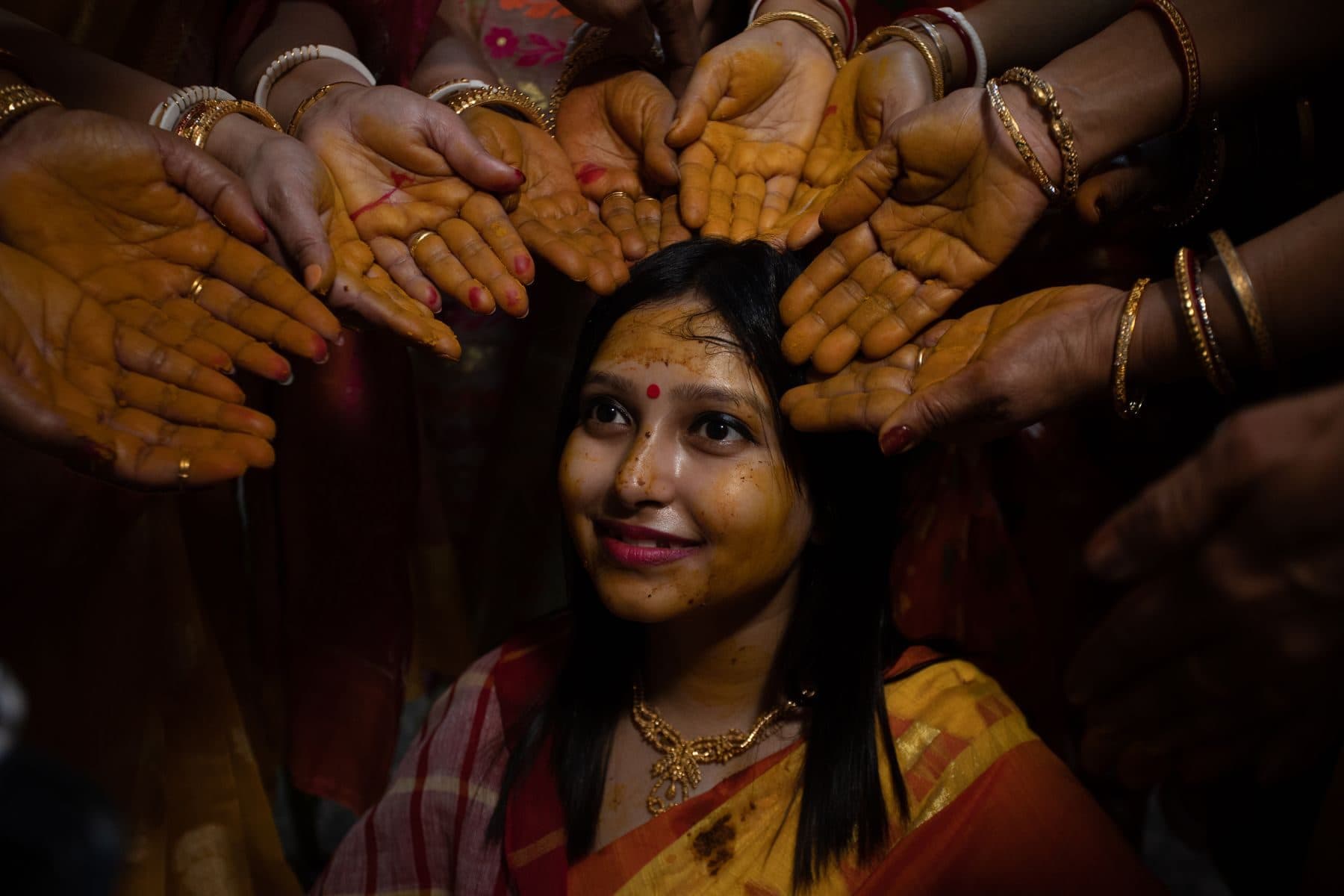 Family hands holding turmeric over a woman in a yellow saree at a haldi