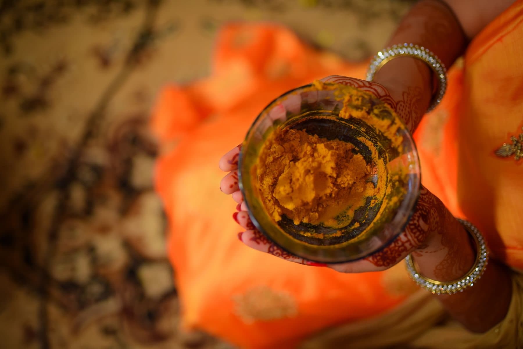 A bowl of haldi held in mehendi-decorated hands over orange silk