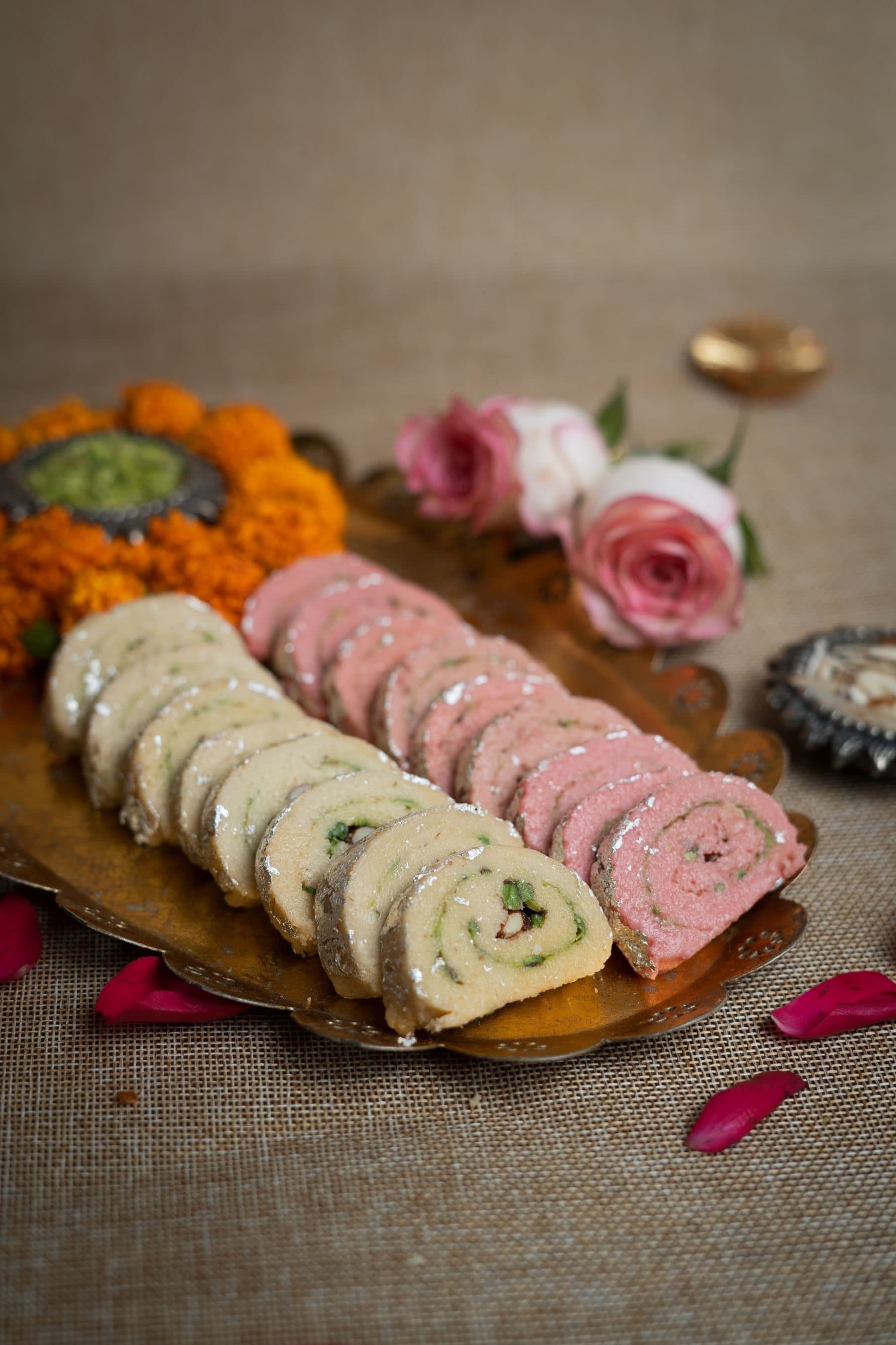 Pistachio and rose mithai rolls with marigolds on a gold tray