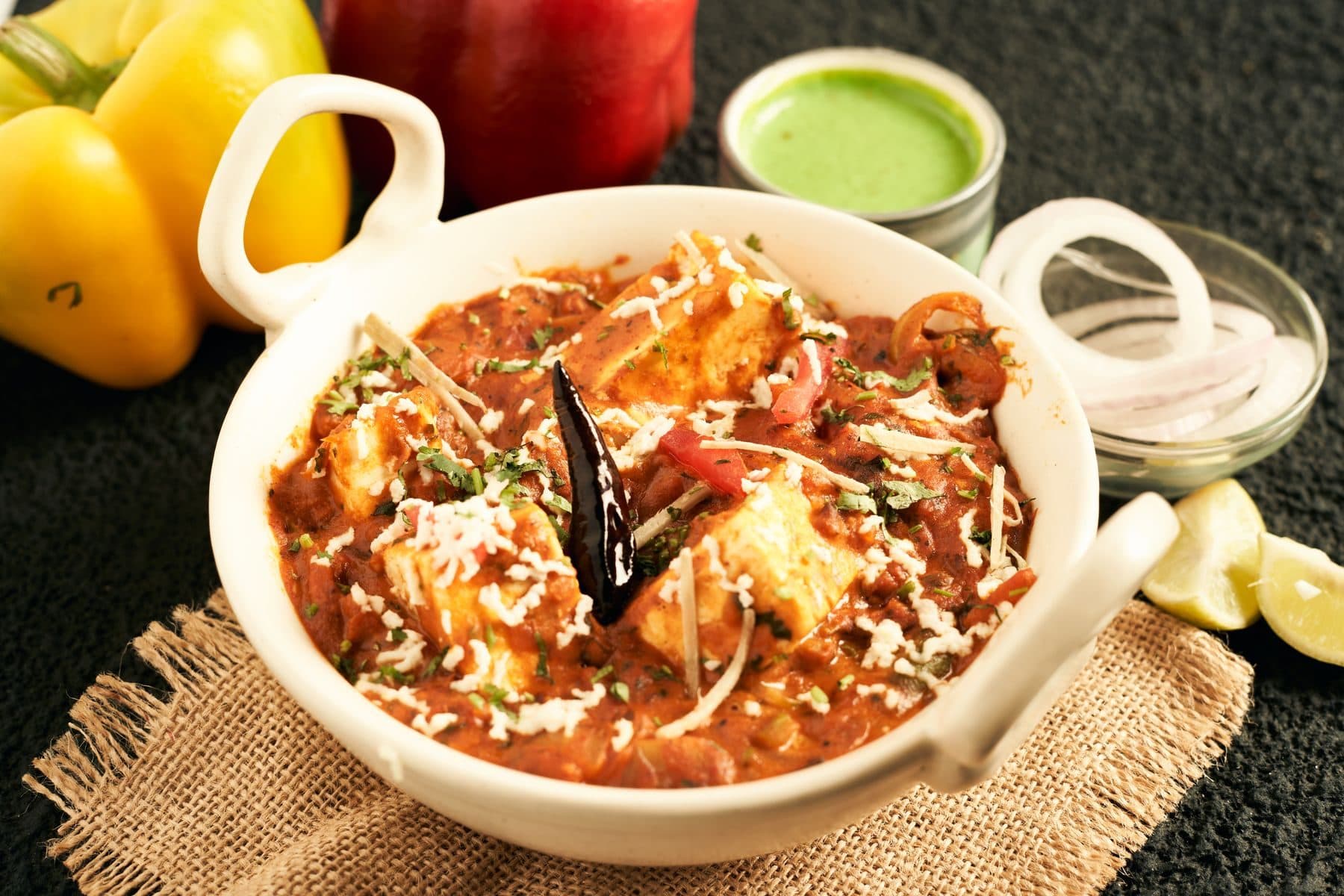 Paneer kadai in a white handi with mint chutney and peppers