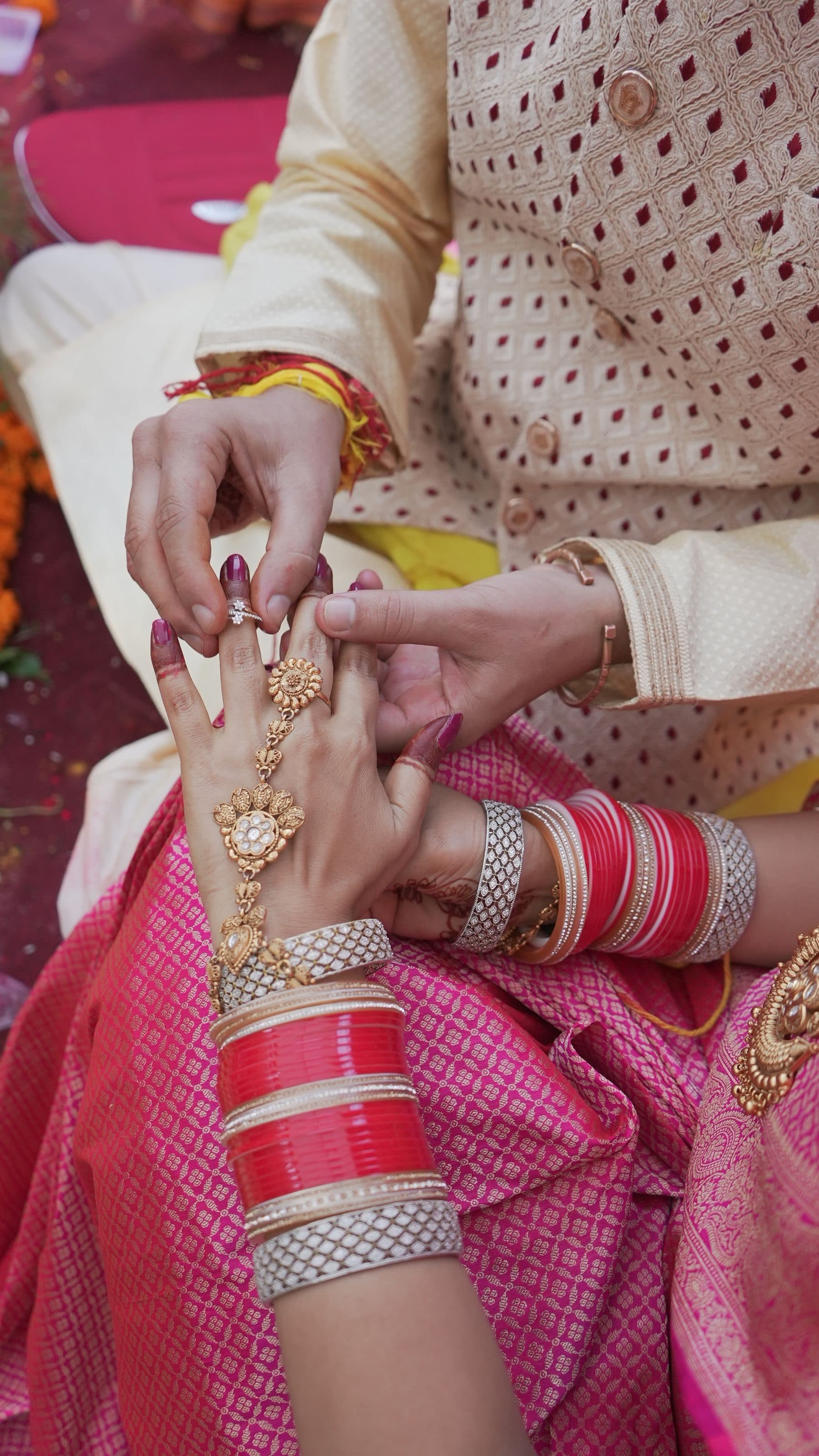 Hands exchanging rings at an Indian engagement, with mehendi and red bangles